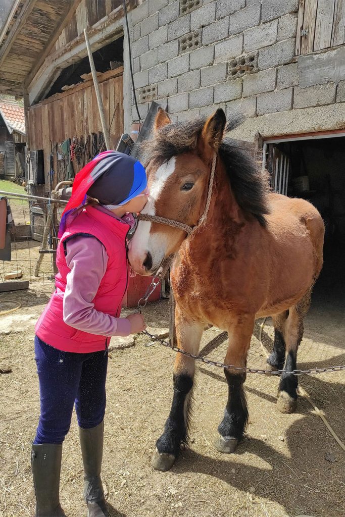 djevojčica u roza jakni ljubi u glavu malog konja